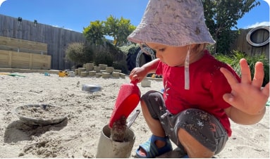 toddler playing with a shovel in sandpit.